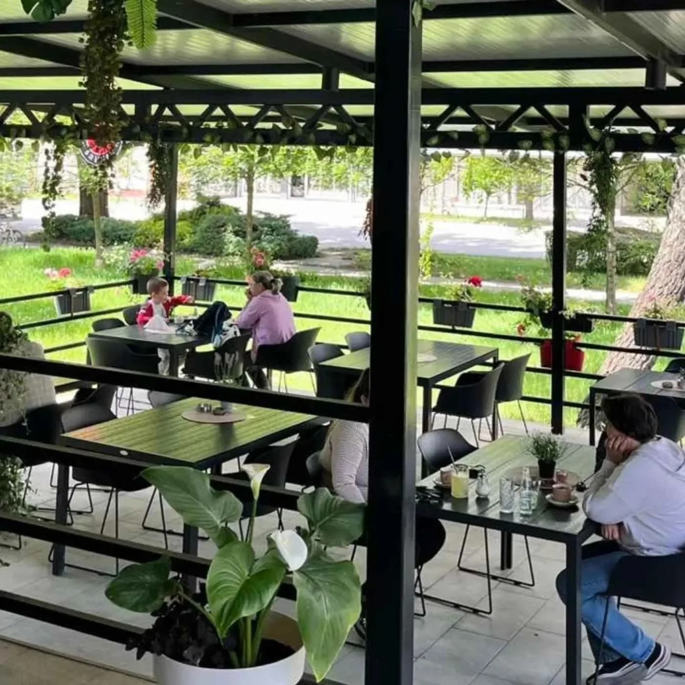 Letnja bašta picerije Aloo Aloo u Sremskoj Mitrovici — natkrivena terasa sa gostima, zelenilom i pogledom na park